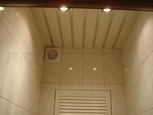 Вид подвесного реечного потолка с встроенными светильниками в туалетной комнате, установка вентилятора, жалюзийной сантехнической дверцы, облицовка стен керамическими плитками с затиркой швов